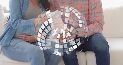 Expectant couple sharing intimate couch moment, woman holding phone and cradling belly