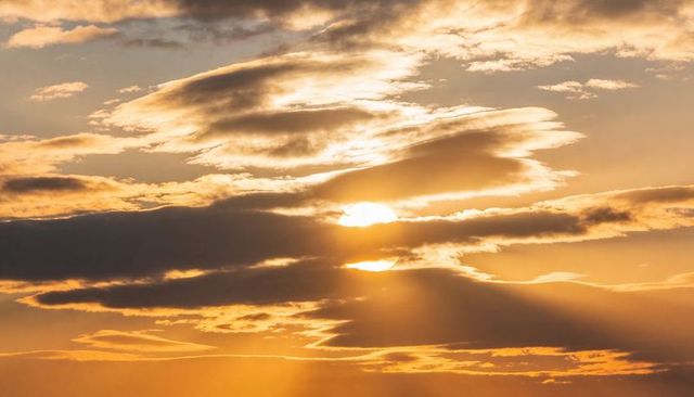 Golden sunbeams piercing layered clouds at sunset creating dramatic atmospheric light
