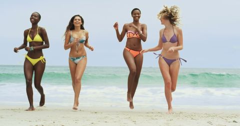 Diverse Friends Running on Sunny Beach in Vibrant Swimwear