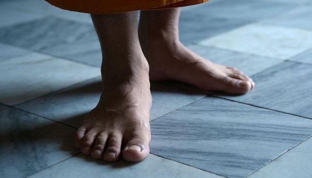 Bare feet standing on cool marble tile with saffron robe hem, serene minimalist scene