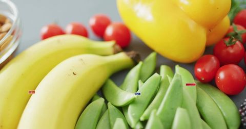 Fresh colorful produce featuring bananas, sugar snap peas, cherry tomatoes, yellow bell pepper