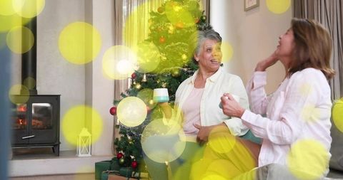 Cozy christmas conversation: two friends chatting with mugs by fireplace and tree