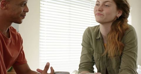 Diverse couple chatting over coffee at home kitchen table in natural window light