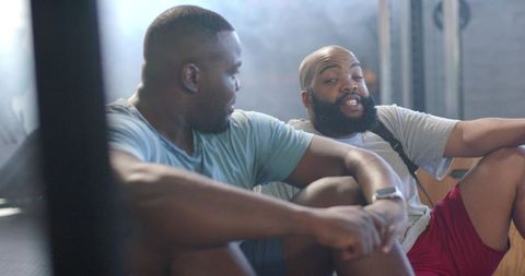 African men resting and chatting after workout in gym, showing camaraderie and recovery