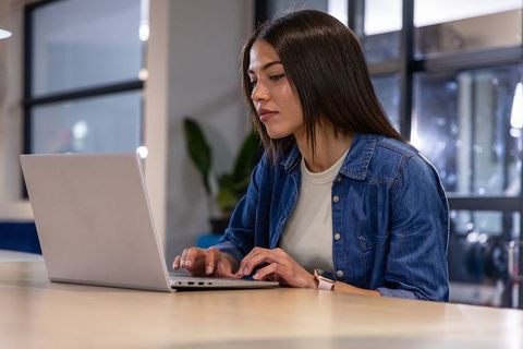 Young woman working on laptop in modern coworking space with denim shirt and smartwatch