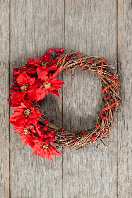 Grapevine wreath adorned with red poinsettias and berries on a wooden plank background. Ideal for holiday-themed projects, rustic decor inspiration, and seasonal marketing materials.