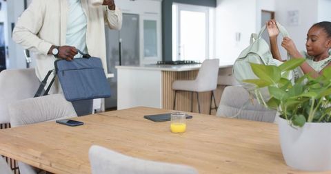 African american father grabbing bag while teen daughter packing backpack at kitchen table