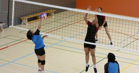 Multicultural women volleyball teams competing, spiking and blocking on indoor court