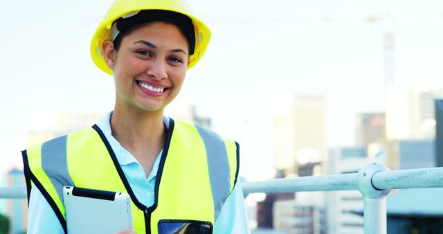 A young, smiling Latina construction worker in safety gear holds a clipboard, with copy space. Her confident demeanor and professional attire highlight the increasing presence of women in the construction industry.