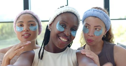African american women wearing blue gel under-eye patches smiling together at home spa