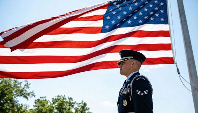 Standing air force honor guard wearing dress uniform beneath waving american flag