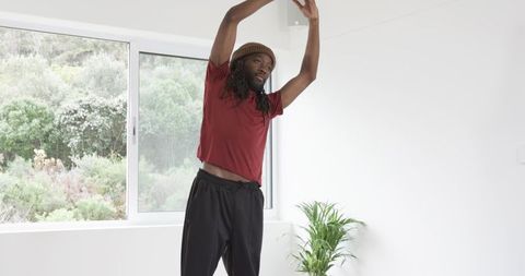African American man stretching by sunlit window in minimalist interior for home wellness