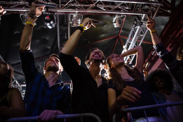 Group of friends enjoying a live performance in a nightclub, capturing the moment with their phones. Ideal for use in articles or advertisements related to nightlife, entertainment, music events, and social gatherings.