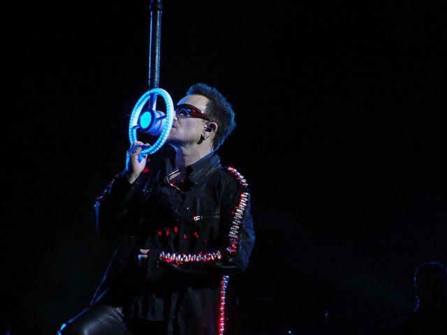 Rock singer performing passionately during a live concert, holding an illuminated hanging microphone. Wearing a leather jacket and sunglasses, contributing to an energetic performance ambiance. Ideal for themes related to music, live performances, rock concerts, and entertainment promotions.