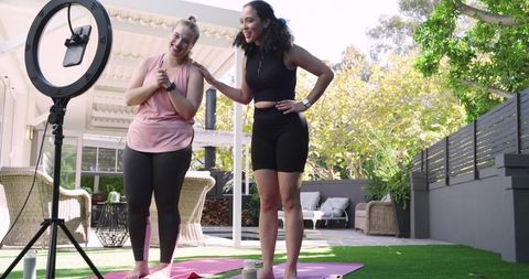 Women recording fitness session on outdoor patio with ring light