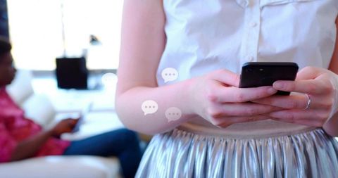 Woman texting on smartphone in living room holding phone close-up with chat bubbles