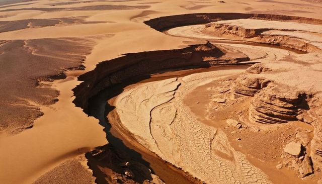 Meandering dry riverbed revealing layered sandstone cliffs and cracked mud desert canyon