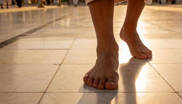 Walking barefoot on sunlit marble courtyard with rolled pant cuffs casting long shadow
