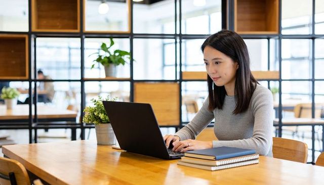 Asian woman working on laptop in bright coworking space for focused productivity and study