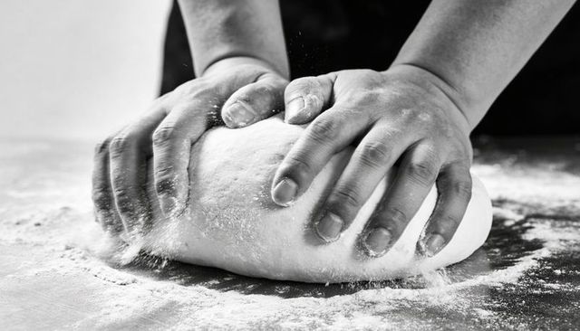 Artisan hands kneading dough on floured counter, monochrome bakery close-up