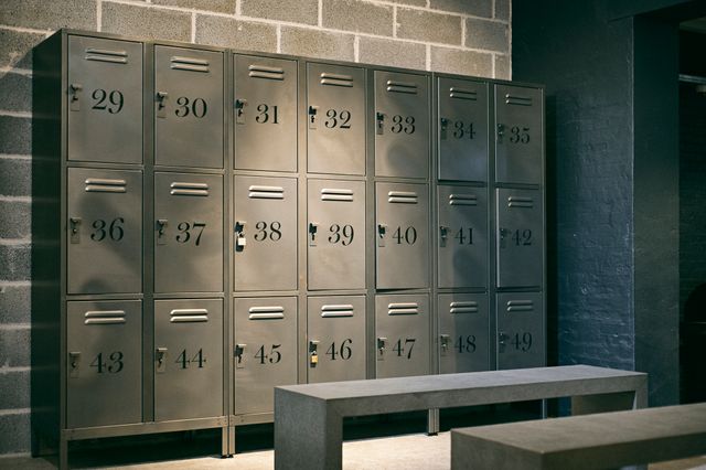 Industrial locker room with gray metal lockers numbered and sturdy benches. Ideal for use in gym, workplace, or storage related topics. Shows organization, security, and minimalistic design, great for illustrating fitness, work environments, and secure storage solutions.