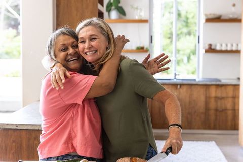 Senior Friends Cooking and Embracing in Home Kitchen