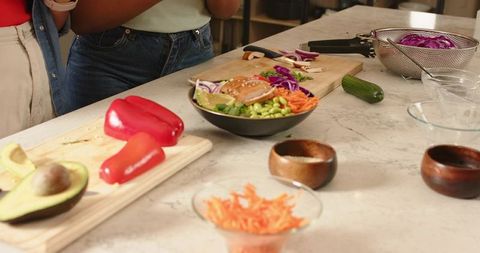 Preparing colorful veggie bowl on marble counter with avocado, red pepper, shredded carrot
