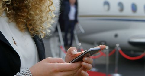 Businesswoman Using Smartphone Near Private Jet at Airport - Download Free Stock Images Pikwizard.com