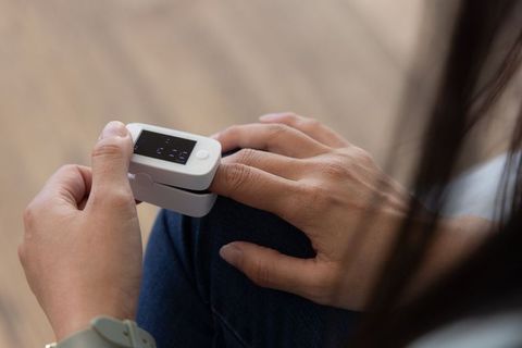 African american mature woman checking fingertip oximeter on knee at home
