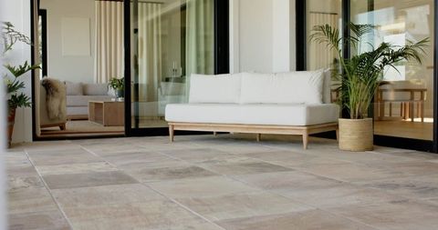 Minimalist outdoor lounge featuring white sofa on stone tile patio with glass sliding doors