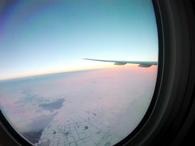 This image portrays a picturesque aerial view of a snow-covered landscape seen through an airplane window during sunrise. The airplane wing and the warm hues of the sky add to the overall beauty of the scene. Ideal for use in travel blogs, airline promotions, winter travel advertising, and content related to exploring new destinations from the air.