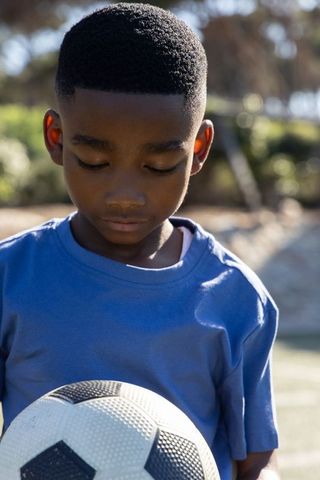 Portrait of african american boy holding soccer ball looking down on soccer field