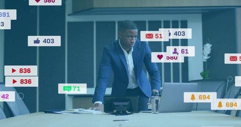 Businessman leaning over laptop in boardroom monitoring analytics and social media notifications