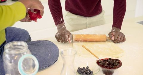African American man and Indian woman rolling dough in kitchen with blueberries and jam