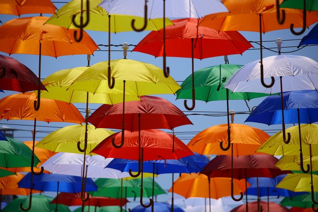 Bright colorful umbrellas hanging against blue sky creating a cheerful visual display. Ideal for articles on unique outdoor decorations, urban art installations and creative summer attractions.
