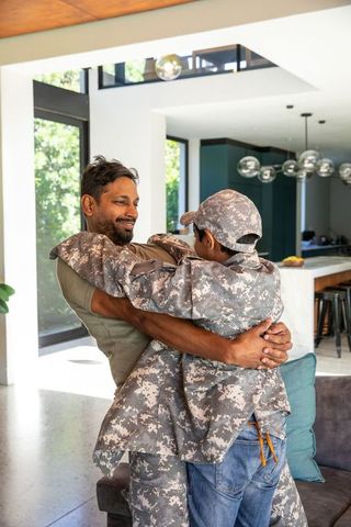 South Asian Father Embracing Teen Son in Camo Uniform at Home