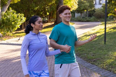 Diverse Couple Walking in Athletic Wear Holding Hands in Park