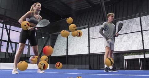 Young athletes practicing paddle sport on modern indoor blue court with floating emoji balls