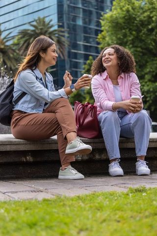 African american friends sitting on urban park bench holding coffee and smiling