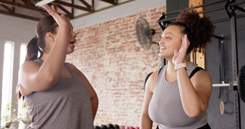 Diverse women high-fiving and chatting in gym workout, smiling friends training together