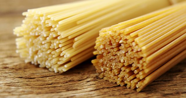 Bundles of uncooked spaghetti lie on a wooden surface, showcasing the texture and form of this popular pasta. Spaghetti is a staple in Italian cuisine and is often used in a variety of dishes, from simple aglio e olio to hearty bolognese.