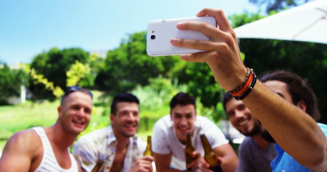 Group of friends enjoying a sunny day outdoors, taking a selfie while holding beers. Ideal for promoting social gatherings, summer events, friendship, and recreation.