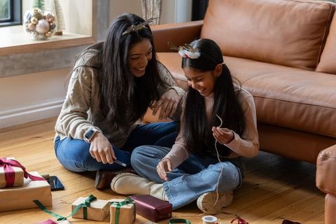 Asian mother and daughter wrapping cozy holiday gifts together on living room floor