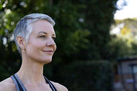 Confident mature woman with short gray hair smiling and gazing outdoors in backyard