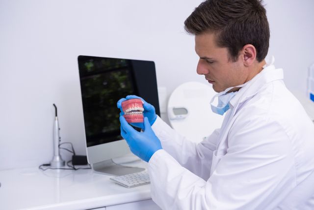 Dentist in white coat and blue gloves examining dental mold in a modern clinic. Ideal for use in articles or advertisements related to dental care, dental technology, healthcare services, and dental hygiene education.