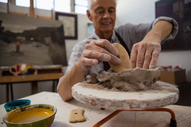 Senior man molding clay in an art class, focusing on his work. Ideal for use in articles or advertisements about senior activities, creative hobbies, art classes, lifelong learning, and pottery workshops.