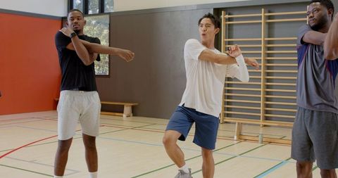 Multiracial men stretching together in indoor gym warming up for group workout routine