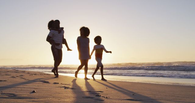 African American family enjoying time together, walking along sandy beach during sunset. Warm sunlight casts long shadows, creating a serene and heartwarming scene. Ideal for concepts of family bonding, leisure, and outdoor activities.