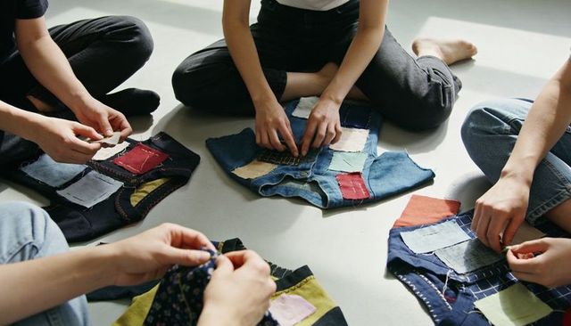 Hands sewing denim patchwork in sunlit craft circle, community textile upcycling