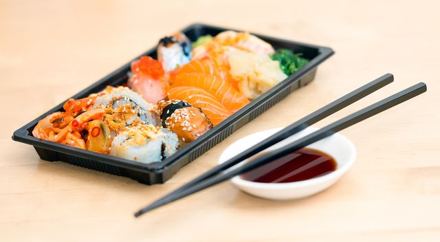 Colorful sushi platter including various types of sushi rolls and nigiri, accompanied by a dish of soy sauce and black chopsticks on a wooden table. Perfect for use in topics related to Japanese cuisine, dining, food presentation, and restaurants.